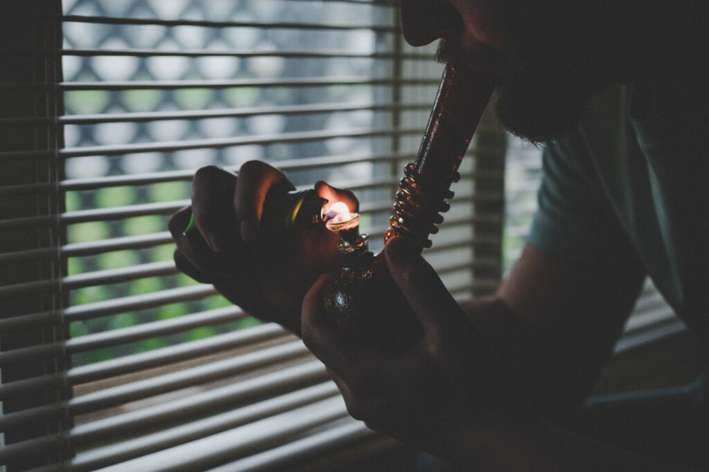 Person Smoking Weed Out Of Bong by Window