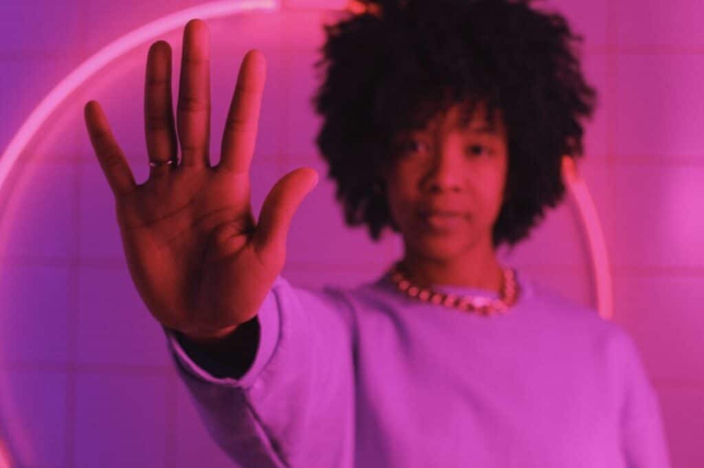 Woman Holding Hand Out Open-Palmed in a Room With Pink Lighting