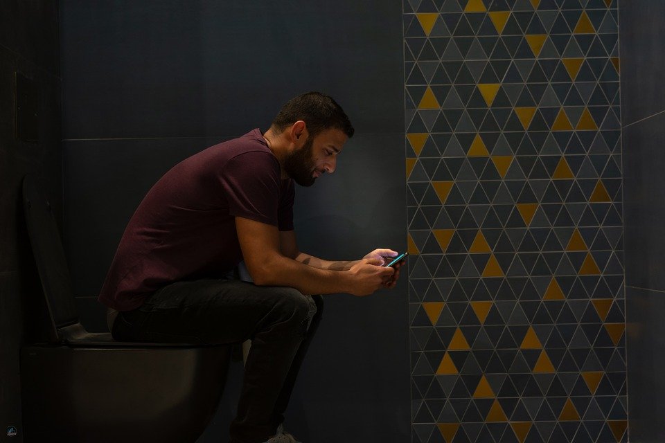 Man Sitting on Toilet Looking at Phone
