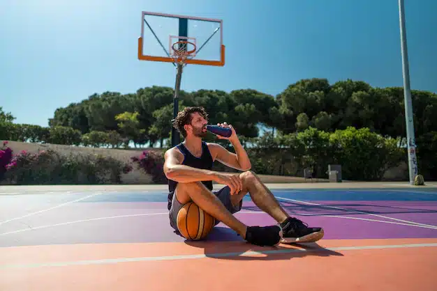 Man Sitting and Drinking Water on a Basketball Court