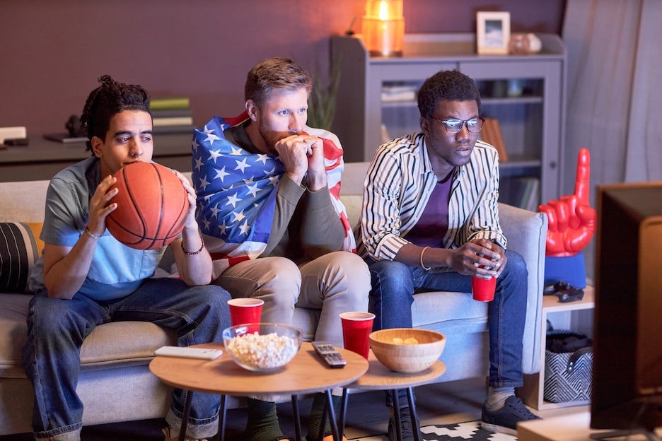 Group of friends watching football match at home with intense face expressions lit by blue light