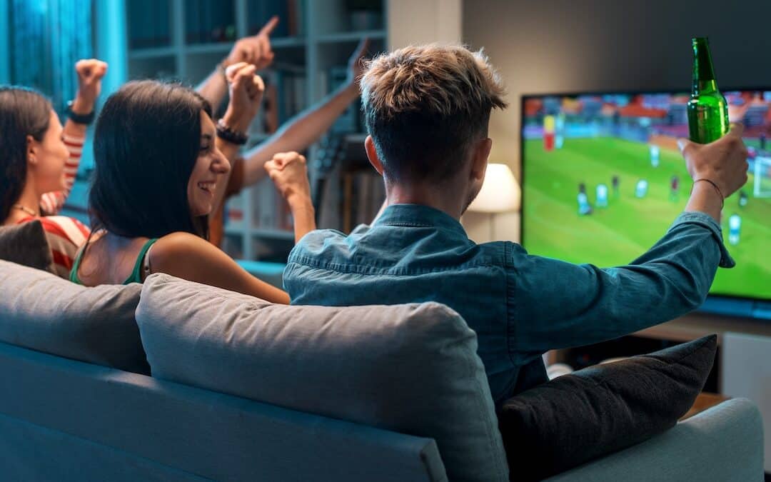 Group of young friends watching a football match on TV together and cheering for their team