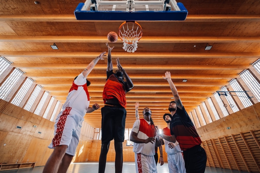 Low angle view of a multicultural basketball team at the basketball hoop throwing a ball. Interracial basketball players in action at the hoop shooting on training on basketball court.Teamwork concept