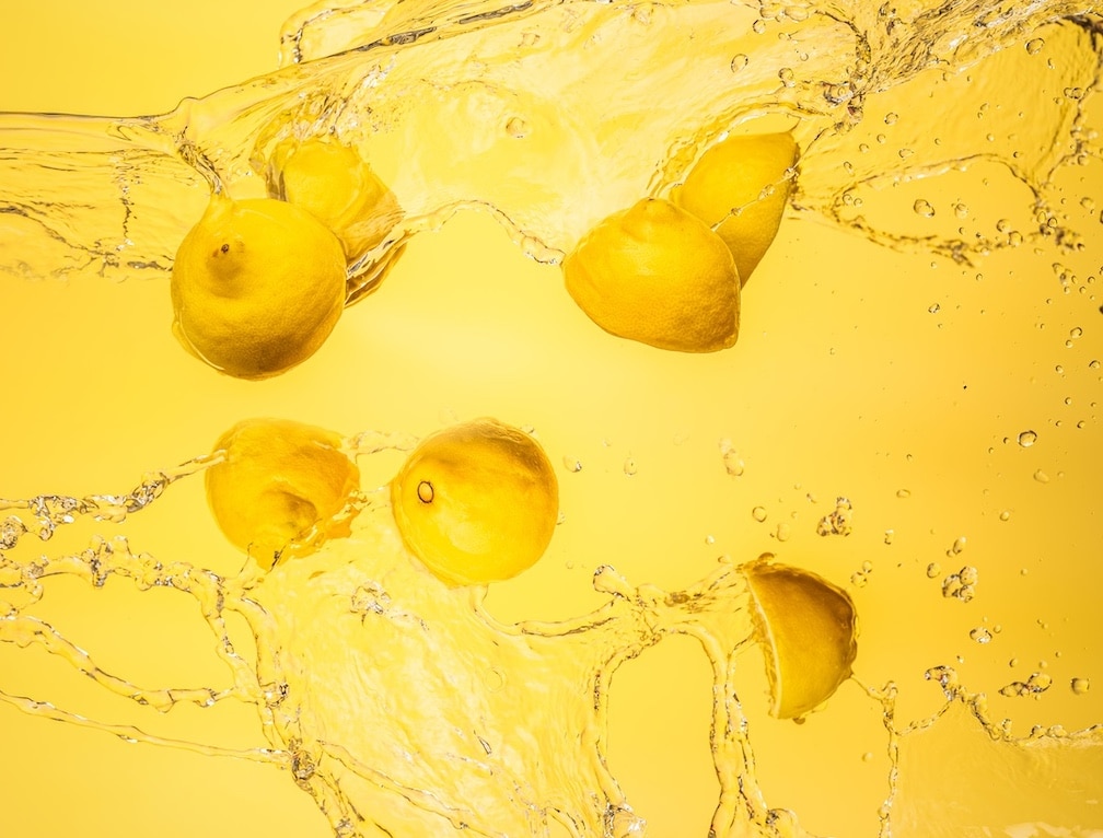 Lemons Being Dropped in Water Against A Yellow Backdrop