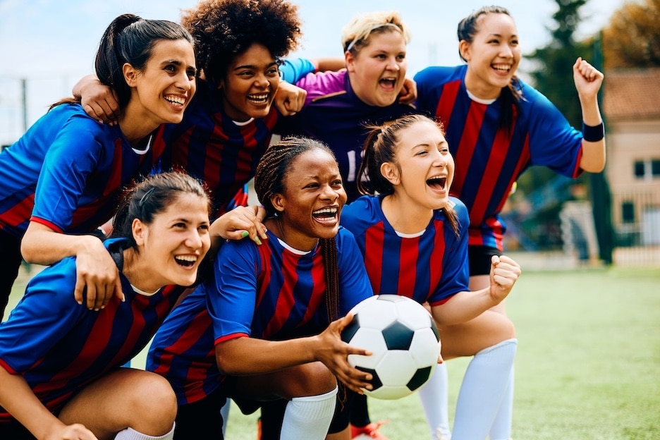 Cheerful women's soccer team celebrating after winning a match at the stadium.