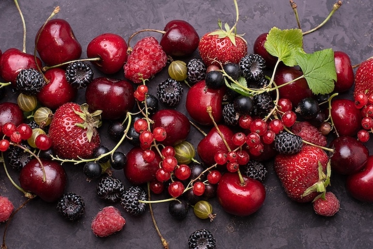 Dark background with scattered summer berries strawberries, currants, raspberries, cherries, close-up.