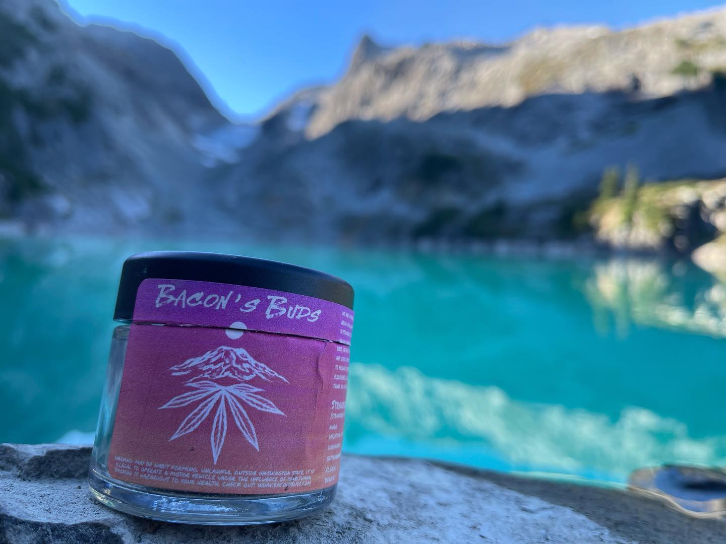 Jar of Bacon's Buds Cannabis on a Mountain in Front of a Blue Lake