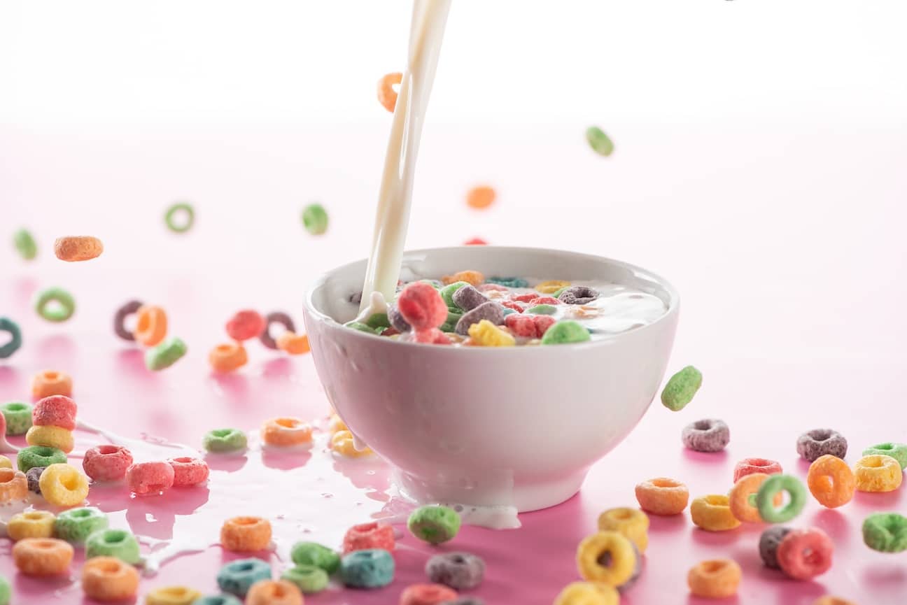 Bright multicolored breakfast cereal in bowl with pouring milk on pink background to represent the strain Cereal Milk