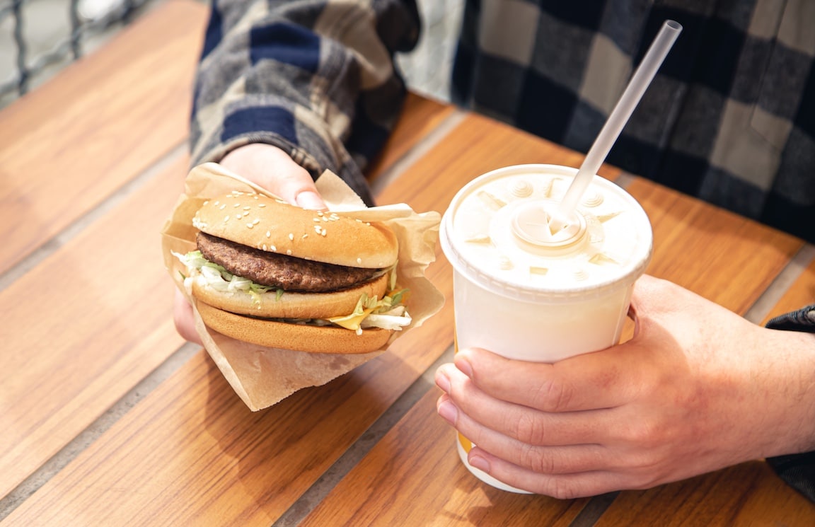 Person with hand on hamburger and drink in fast food cup