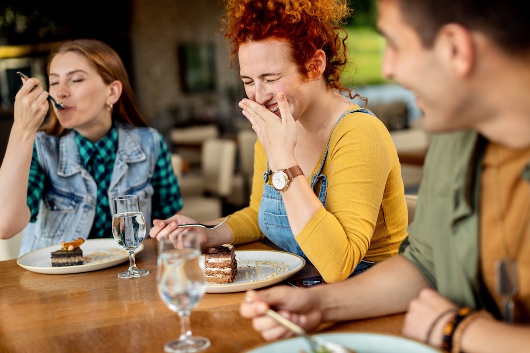 Happy woman laughing and having fun with her friends while eating cake in a cafe