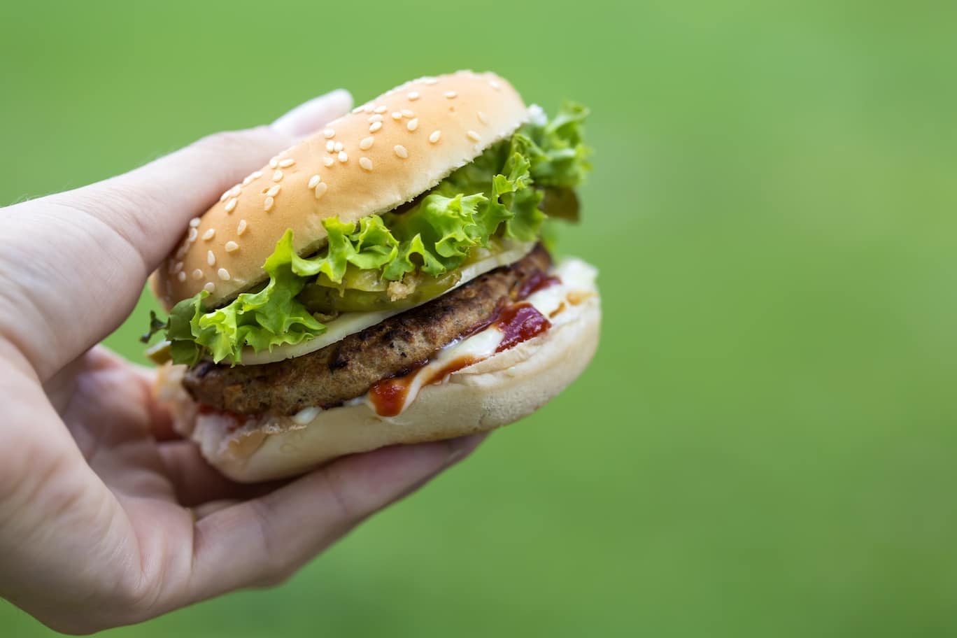 Cheeseburger in hand over green background
