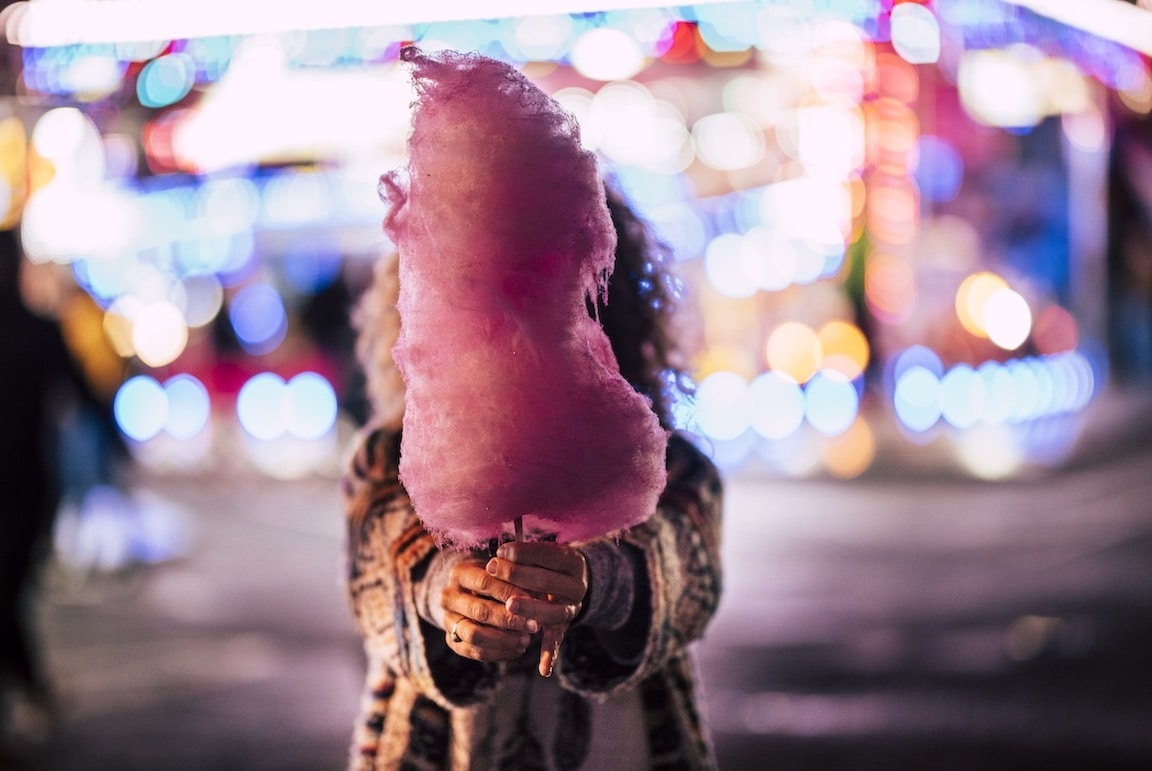Person holding cotton candy in front of their face at a fair carnival