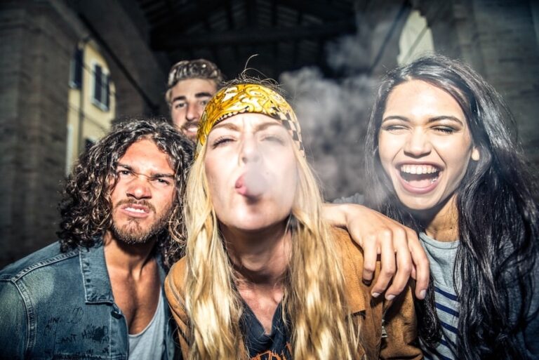 Group of friends looking at camera as one blows smoke forward