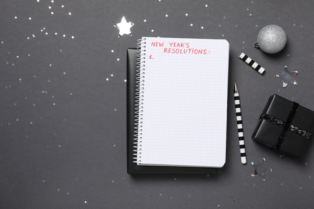 Gift boxes and notepad with list on gray background, space for text New Year's Resolutions