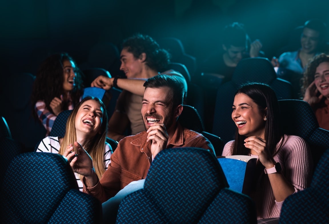 Group of cheerful people laughing while watching movie at the theater
