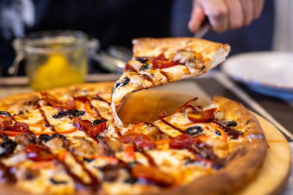 Hand of man holding slice of pizza over the table against restaurant background