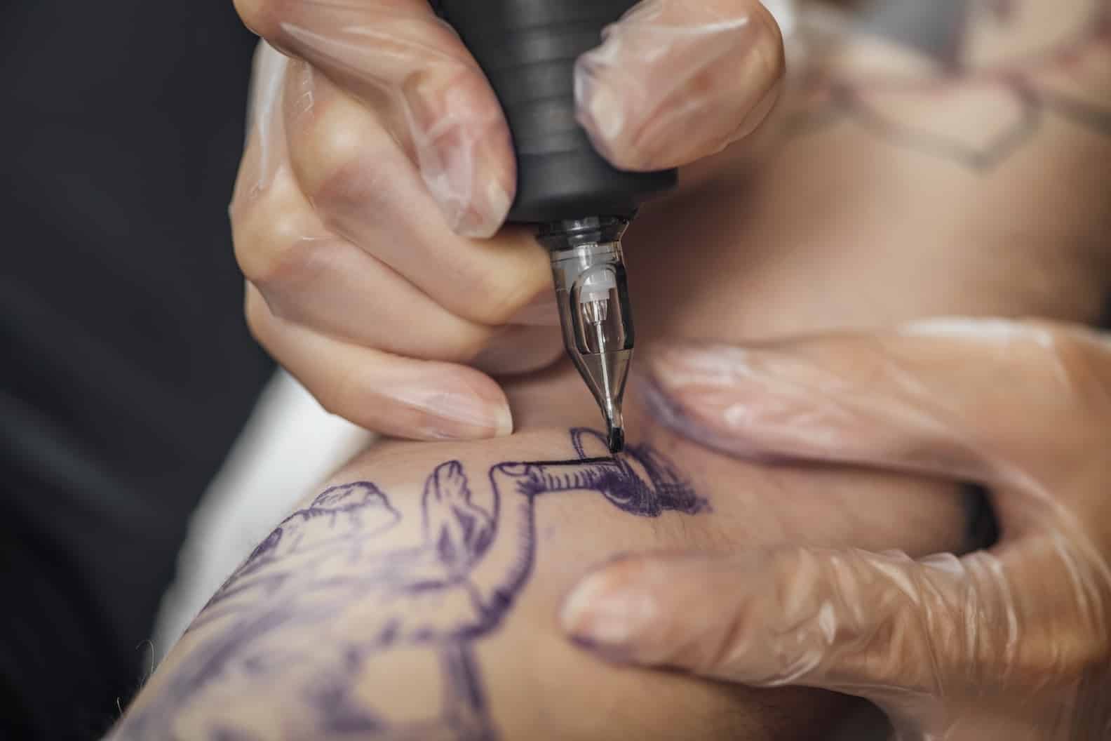 Hand of tattooist in rubber gloves drawing a tattoo with electric tattoo gun, close-up