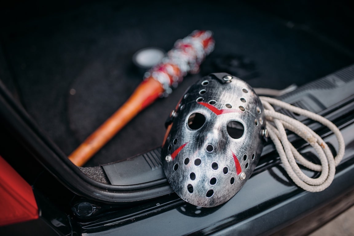 Hockey mask, baseball bat wrapped with bloody metal chain, duct tape and rope closeup, serial murderer concept. Psycho man instruments in opened car trunk, maniac