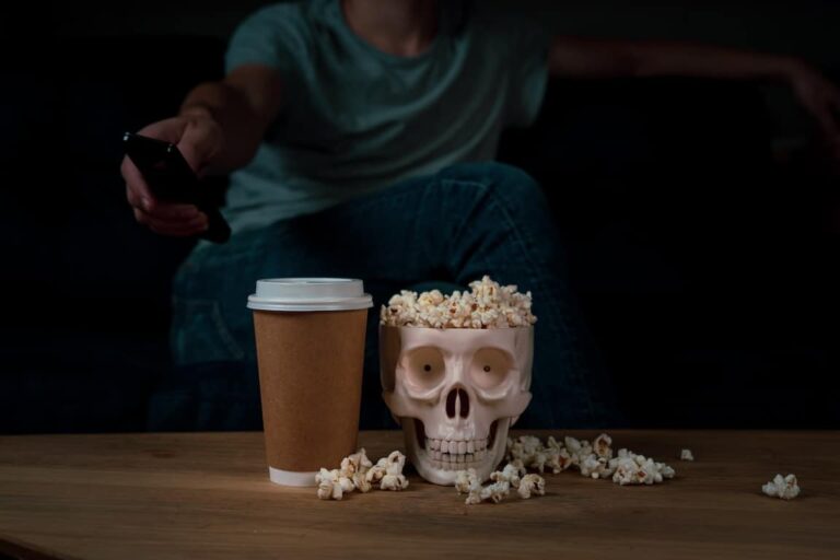 Skull full of popcorn next to coffee cup with a woman holding a remote in the background