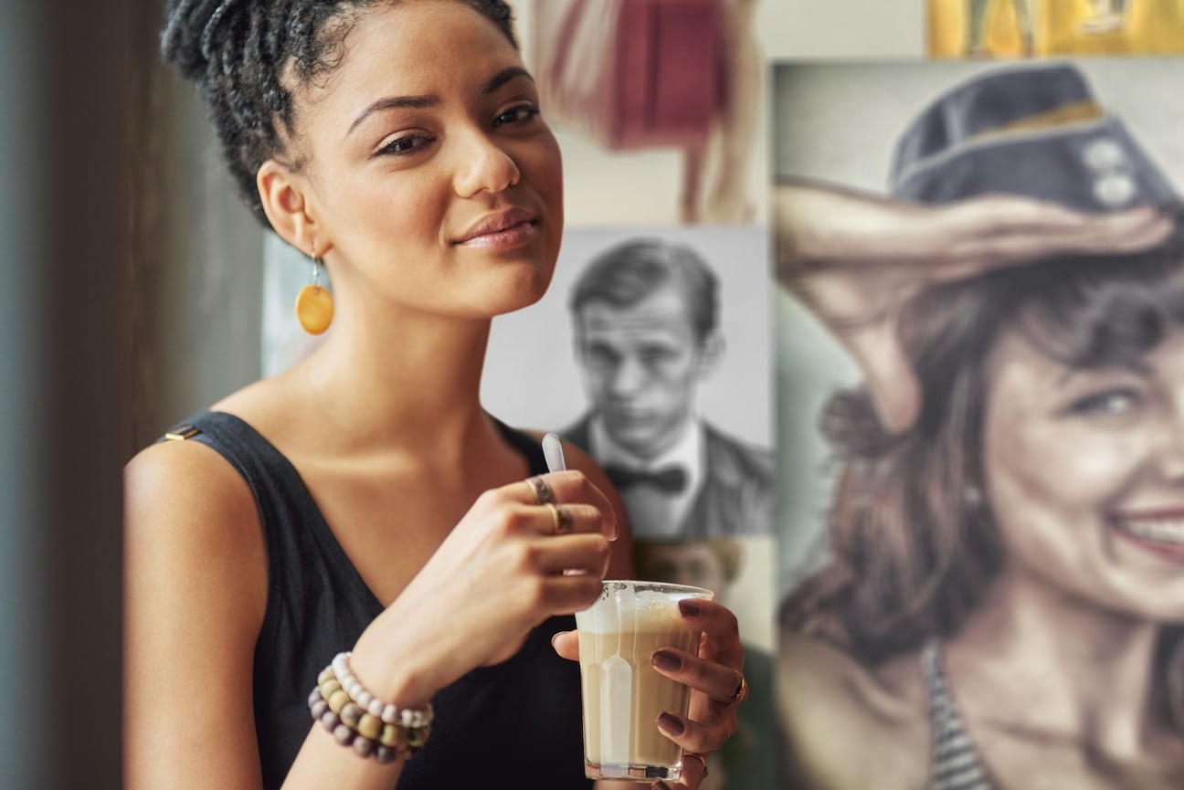 Woman sipping coffee with paintings behind her