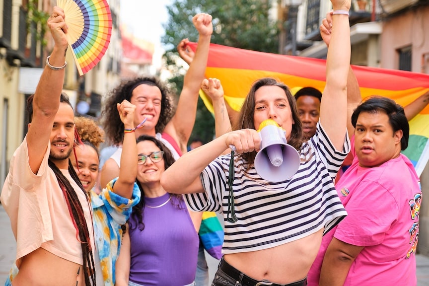People holding pride flags with person in front of holding megaphone; Celebrating LGBTQIA2S+ Pride parade