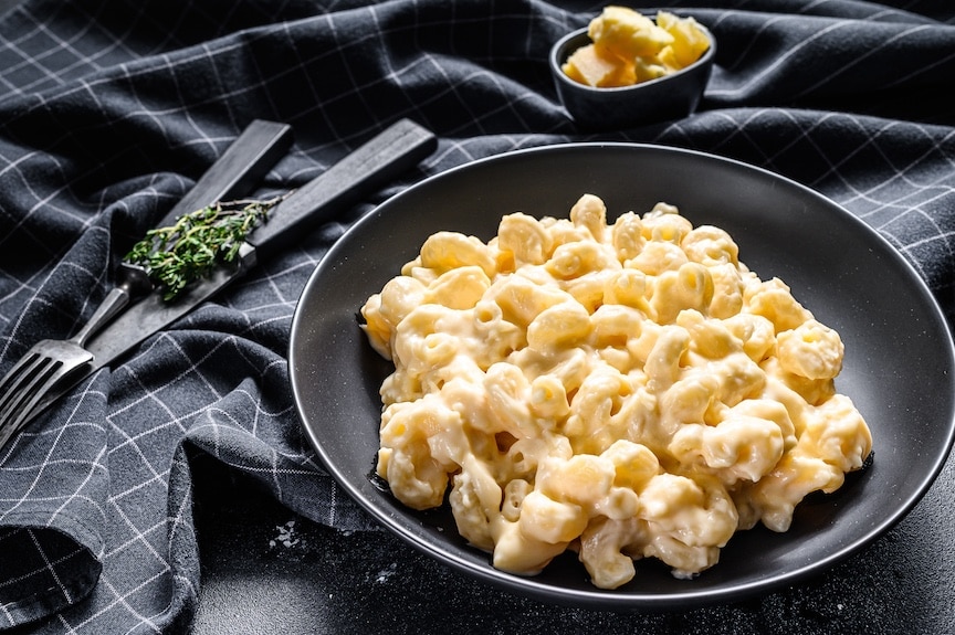 Mac and cheese, macaroni pasta in cheesy sauce. BLack background. Top view