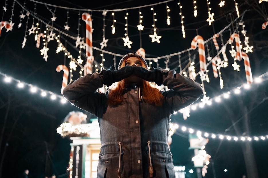 Woman putting hands over her mouth while looking up at Christmas lights