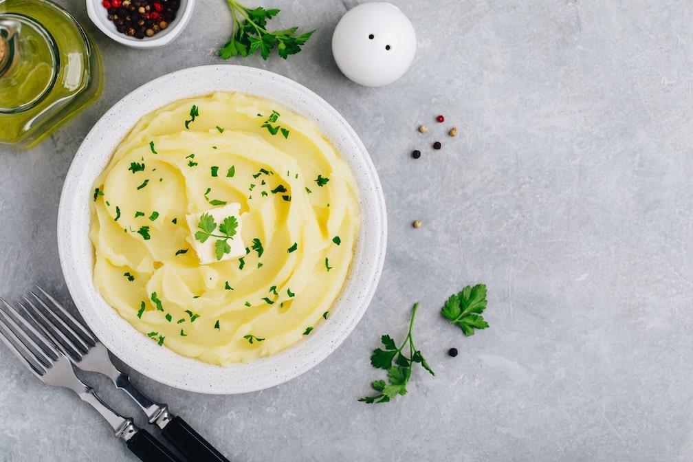 Mashed Potatoes with butter and fresh parsley in a white bowl on gray stone concrete background. Top view