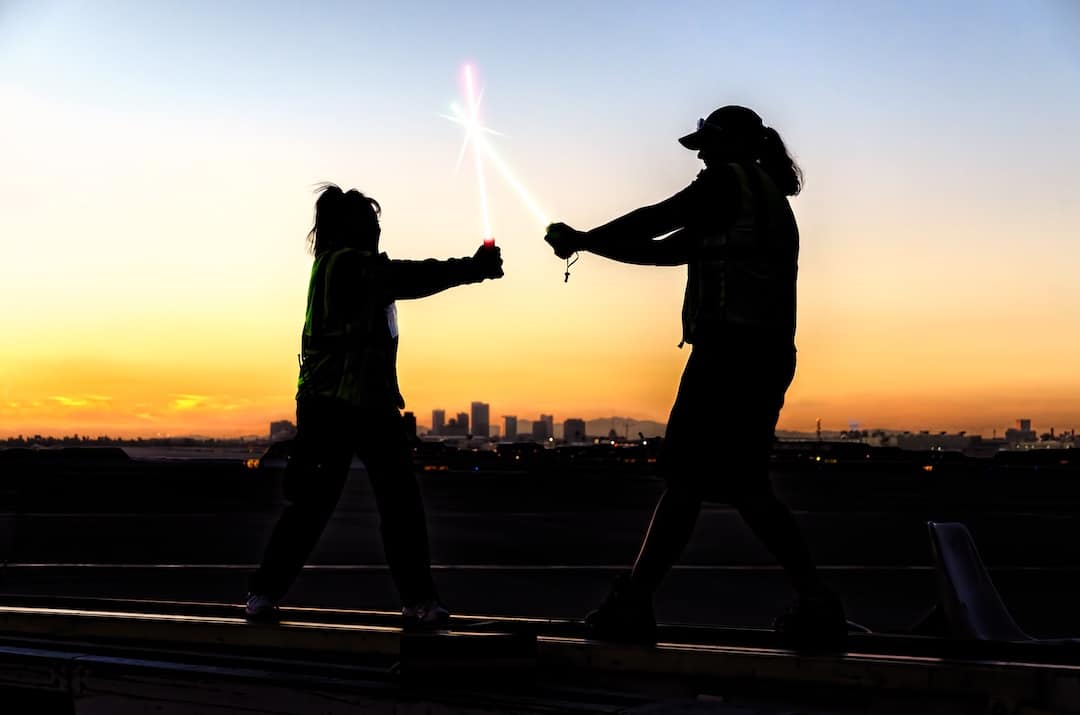 Silhouettes of people playing with lightsabers against a cityscape sunset