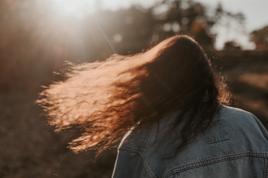 Person with long curly hair blowing to the left from the back