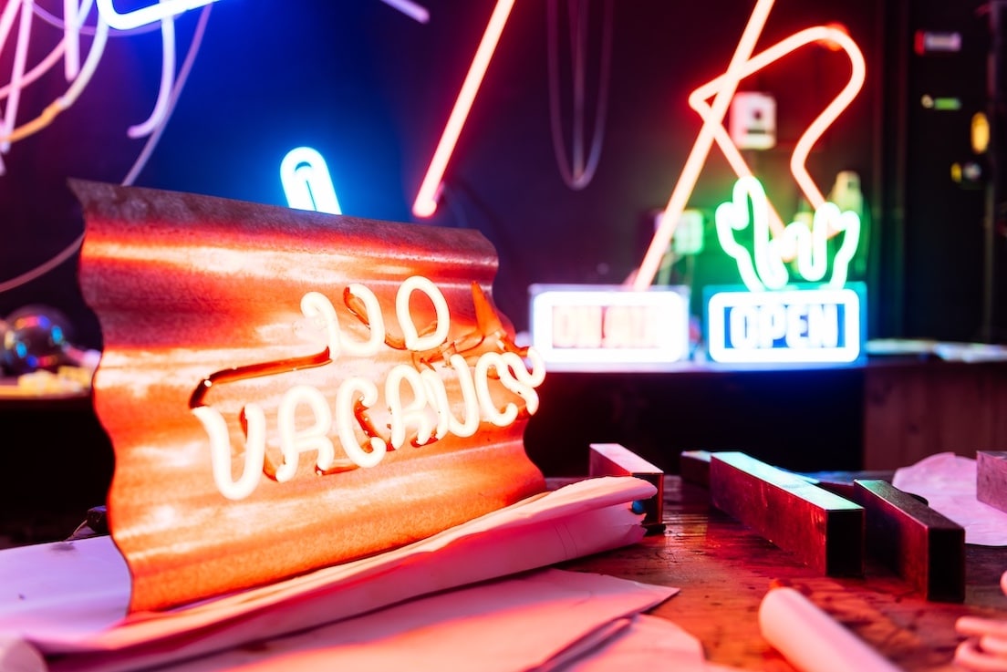 A close-up of a neon sign that reads No Vacancy in a neon sign workshop with other neon signs in the background.