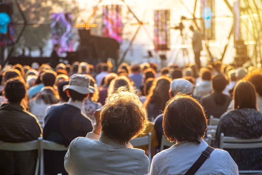 Street concert in the park in summer backs of spectators sitting on chairs at the stage