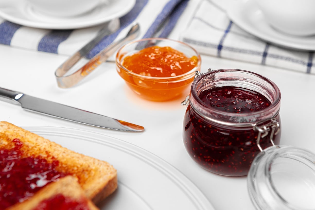 Fruit jams to the side of a butter knife and a piece of toast