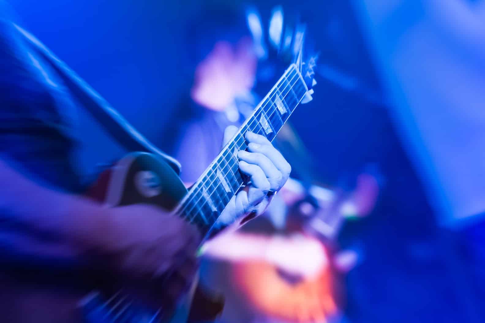 musician playing an electric guitar under blue stage lighting