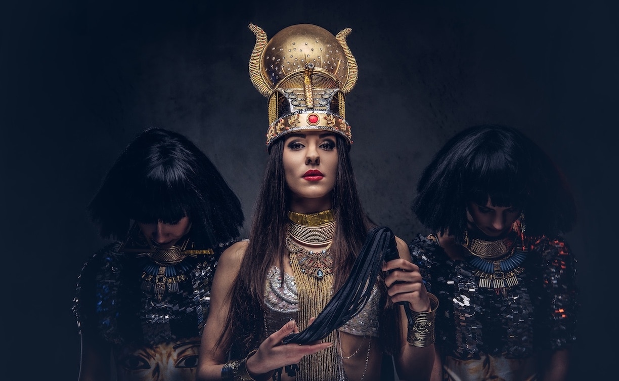 Woman dressed as Egyptian royalty with two people bowing their heads in the background