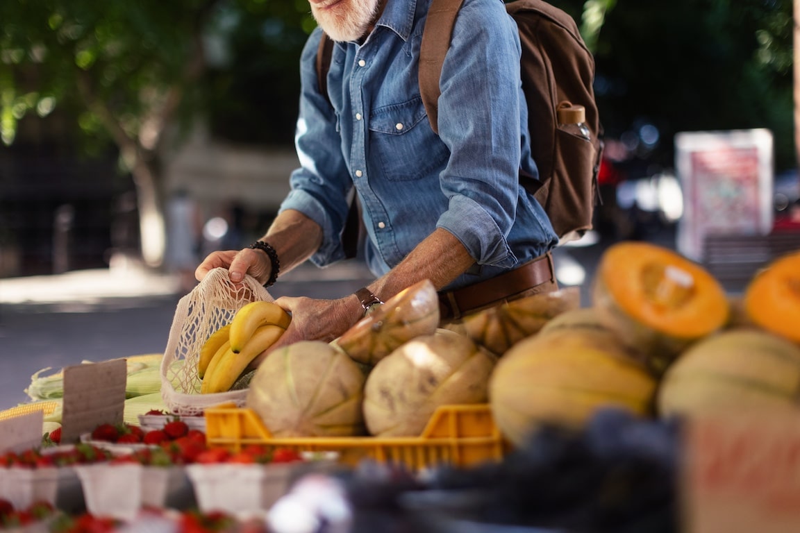 Portrait of senior man shopping at market in the city. Elderly man buying fresh vegetables and fruits from market stall