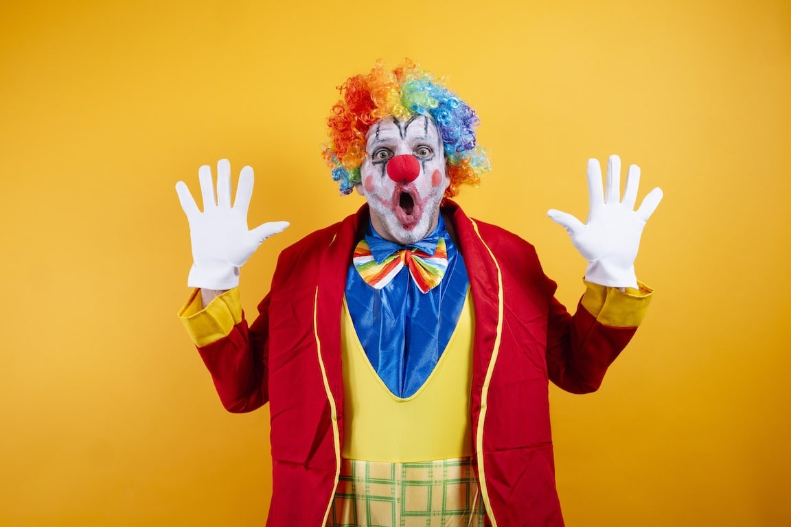 Shocked clown with rainbow wig, wide-eyed, hands up
