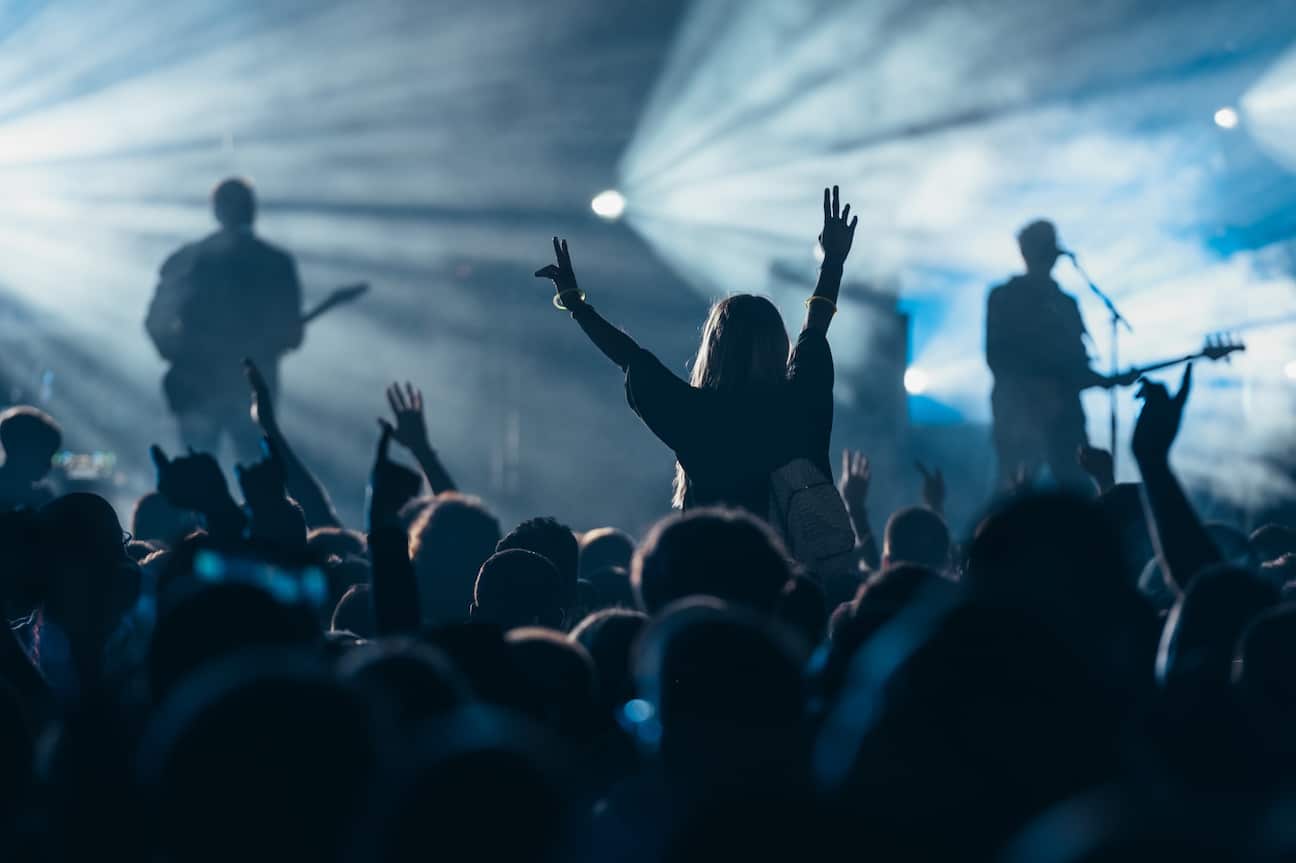 Stage lights against woman with with arms raised while enjoying a concert on a music festival. Crowd with raised hands.
