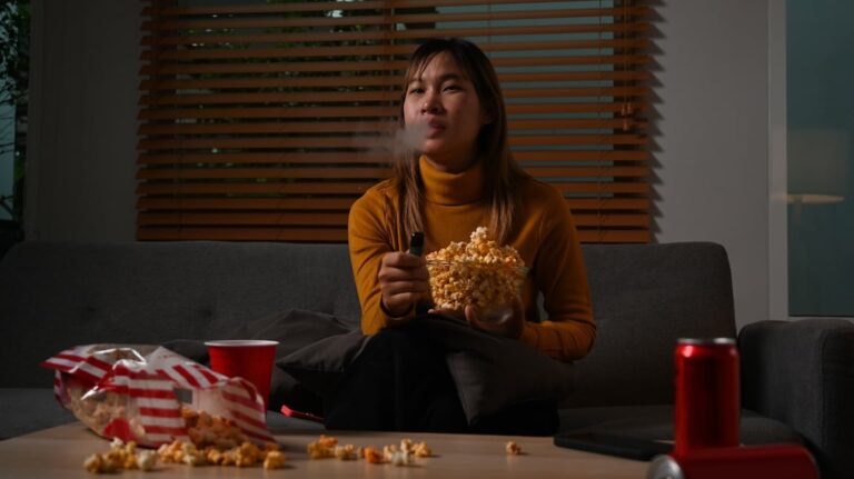 Woman vaping as she eats popcorn and watches a movie