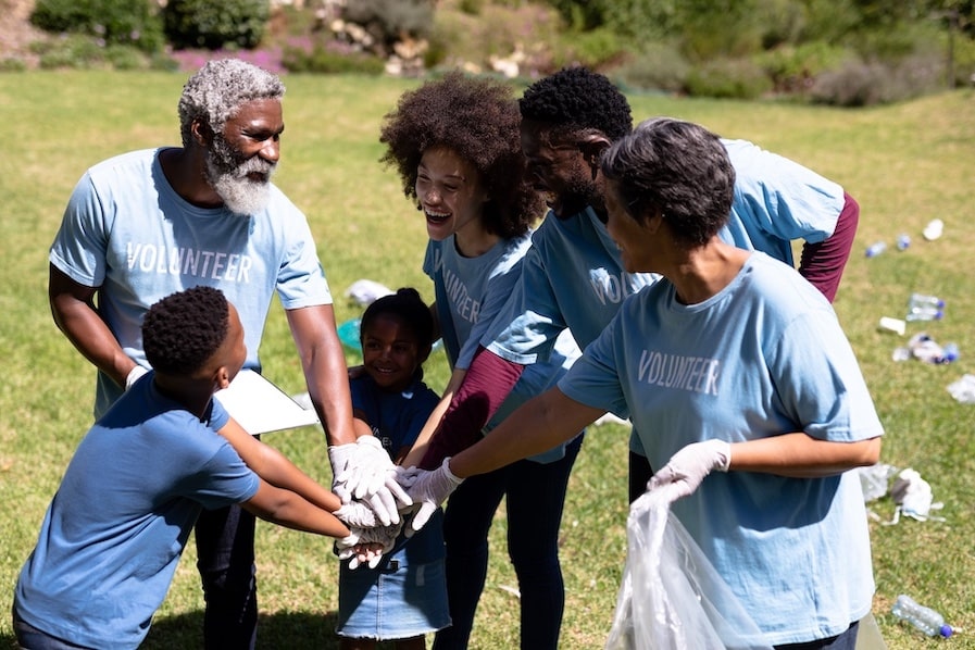 Group of volunteers in a park. Their hands are all joined together in the center of a huddle