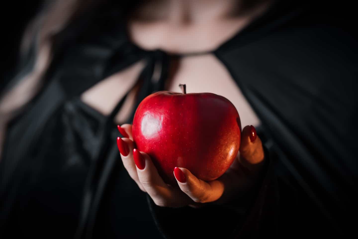 Witch in black holding an apple out to the camera
