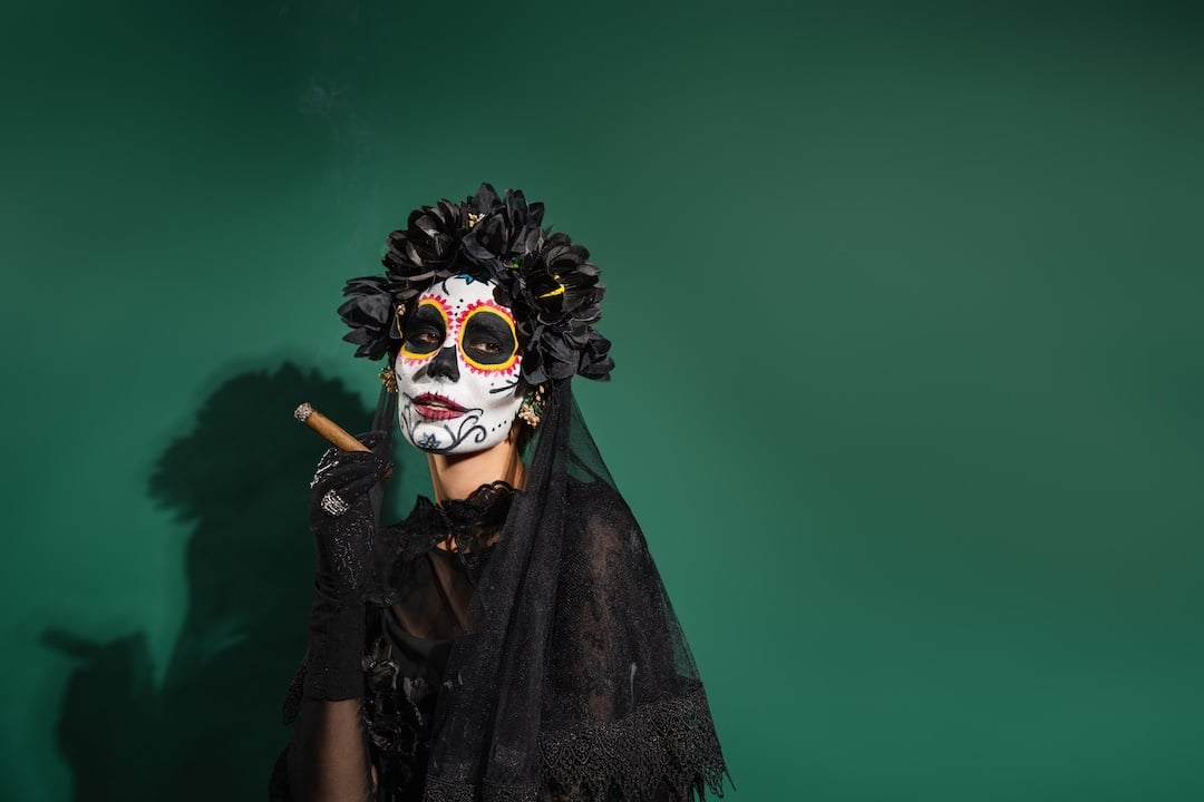 Woman in day of death halloween costume holding cigar on green background