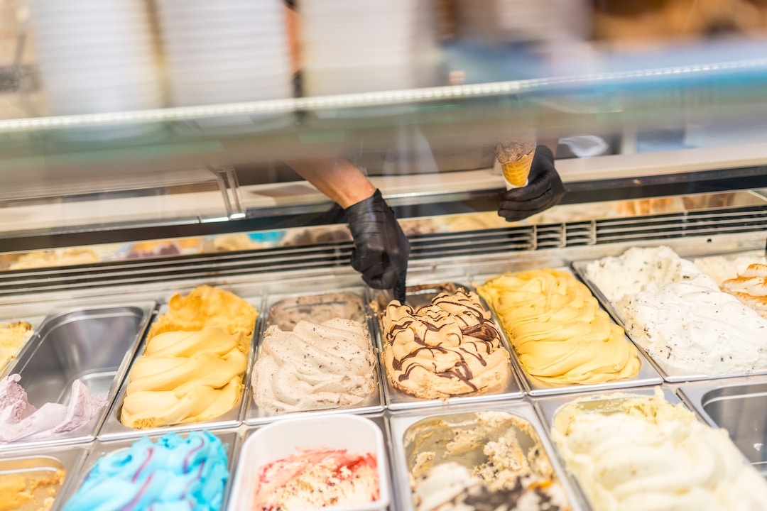 Hands scooping gelato from a selection of different ice cream options